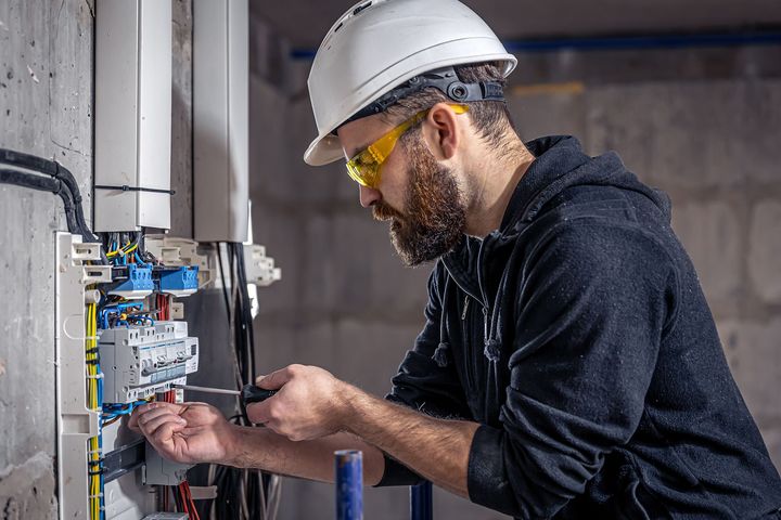 Technician in hard hat wiring an electrical panel indoors