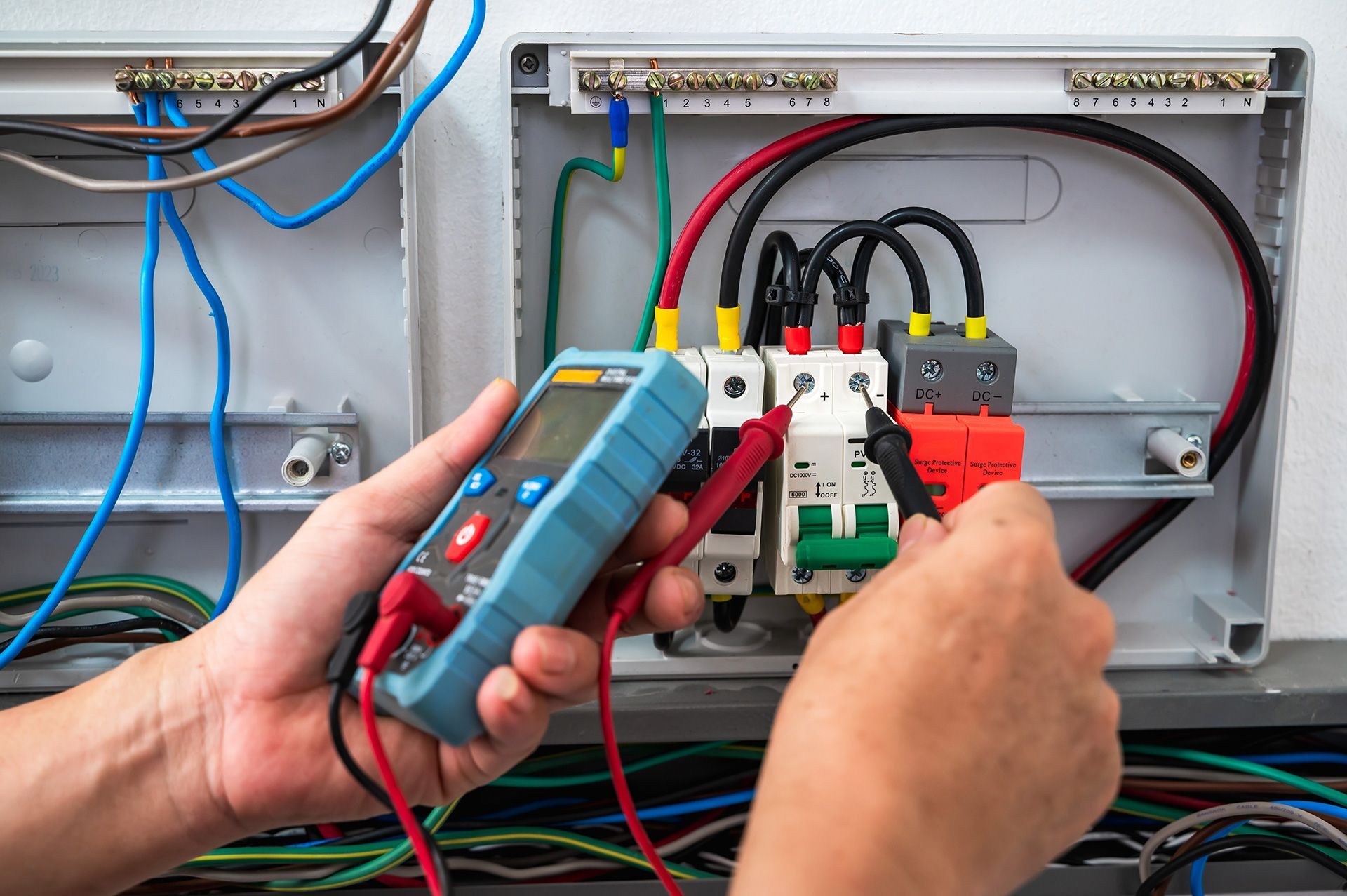 Electrician testing wiring in an open electrical panel with a multimeter and screwdriver.