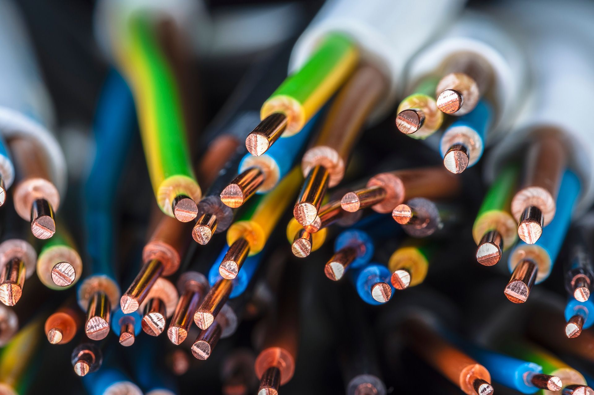 Close-up of many exposed electrical wires with copper ends and colorful insulation against a dark background