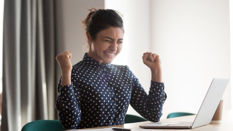 WOMAN AT HER DESK CELEBRATING PROGRESS