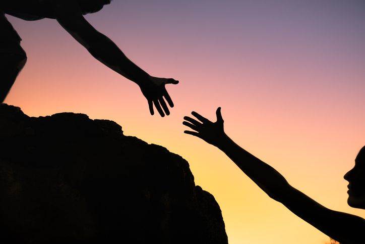 One person giving another a hand as they climb a mountain together