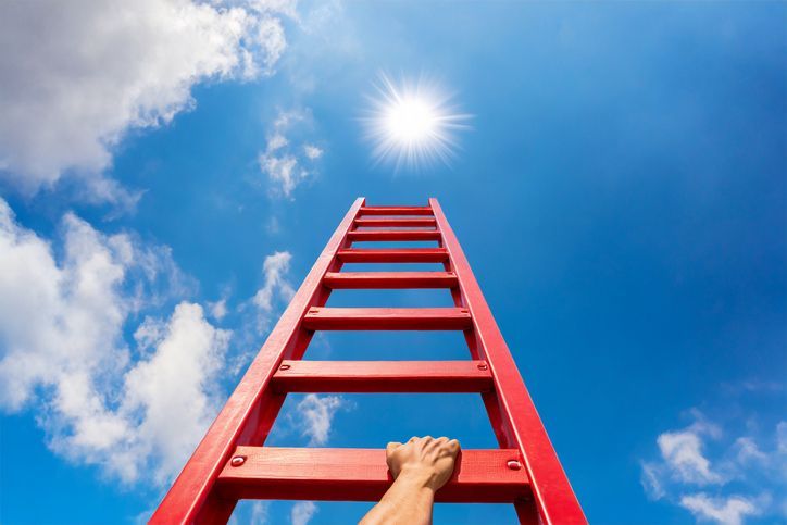 View of a red ladder reaching to the sky; man's hand shown climbing