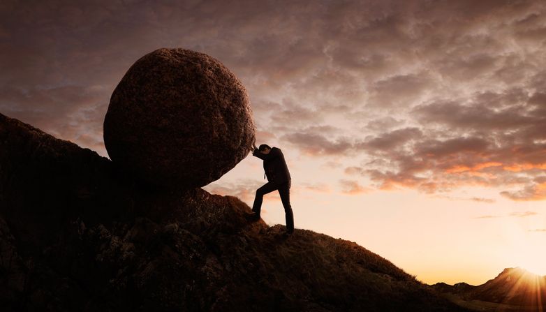 Man pushing an overwhelmingly large rock up a hill.
