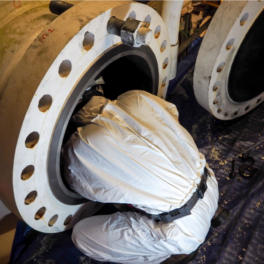 A man in a white suit is working on a pipe