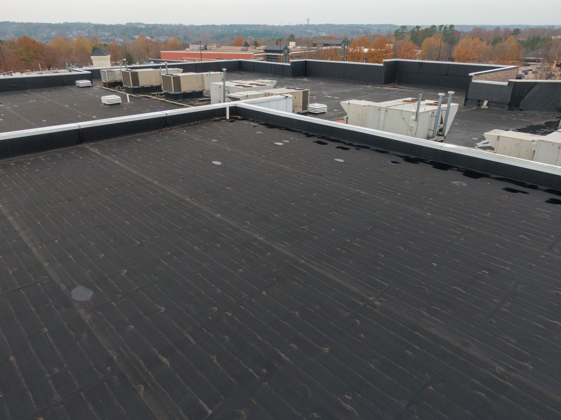 Black flat roof with metal edging, other rooftop equipment visible in background.