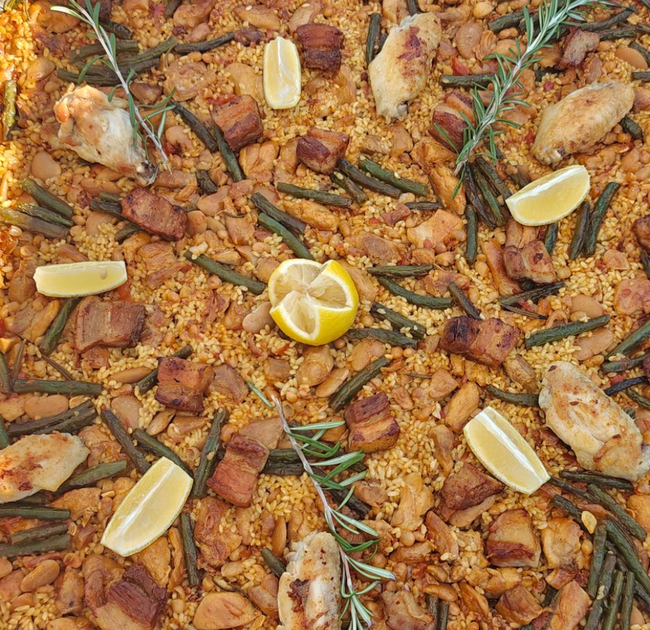 Paella in a large black pan, garnished with lemon wedges.