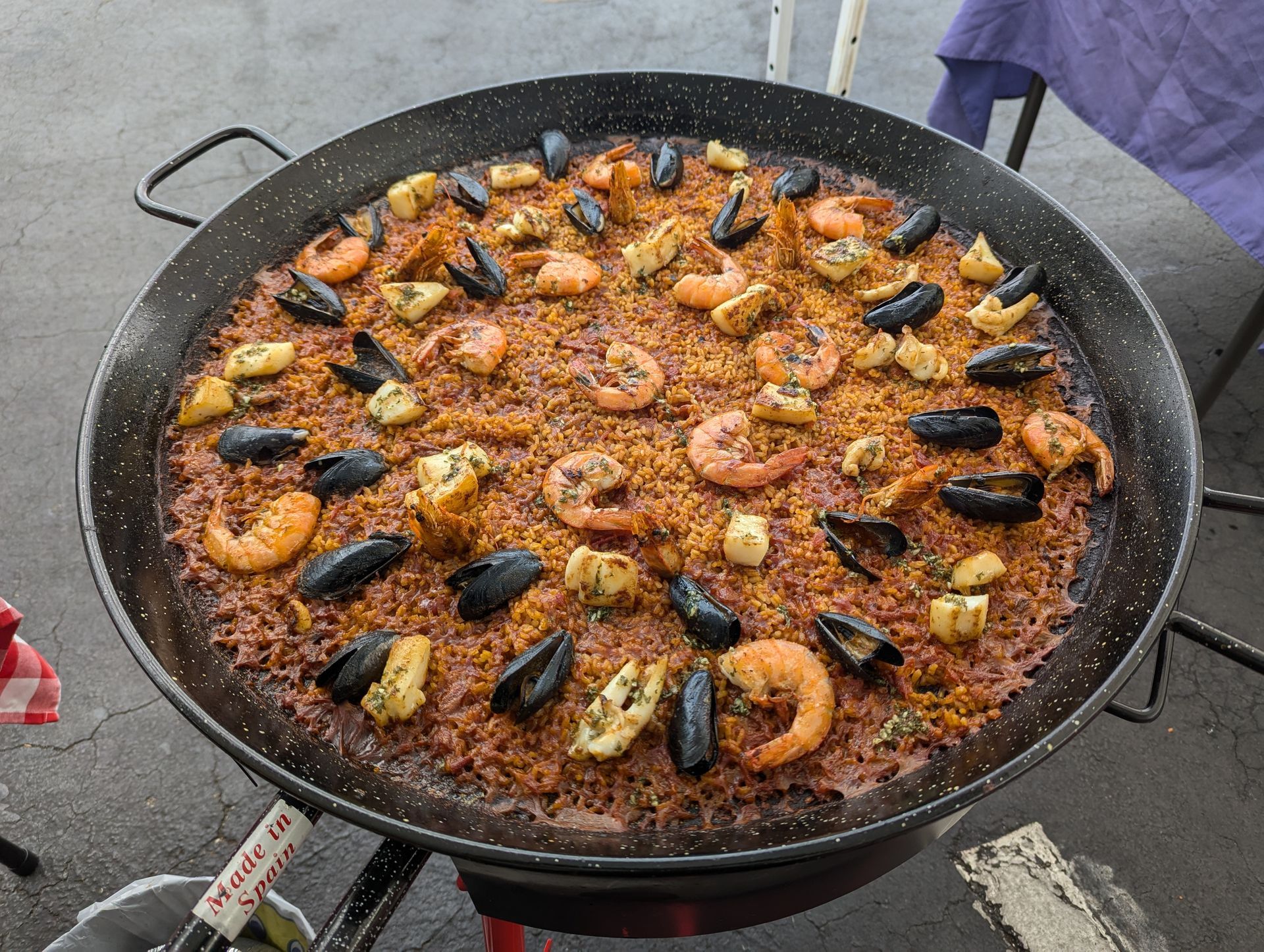 Paella in a large pan with shrimp, mussels, and rice on a grill.