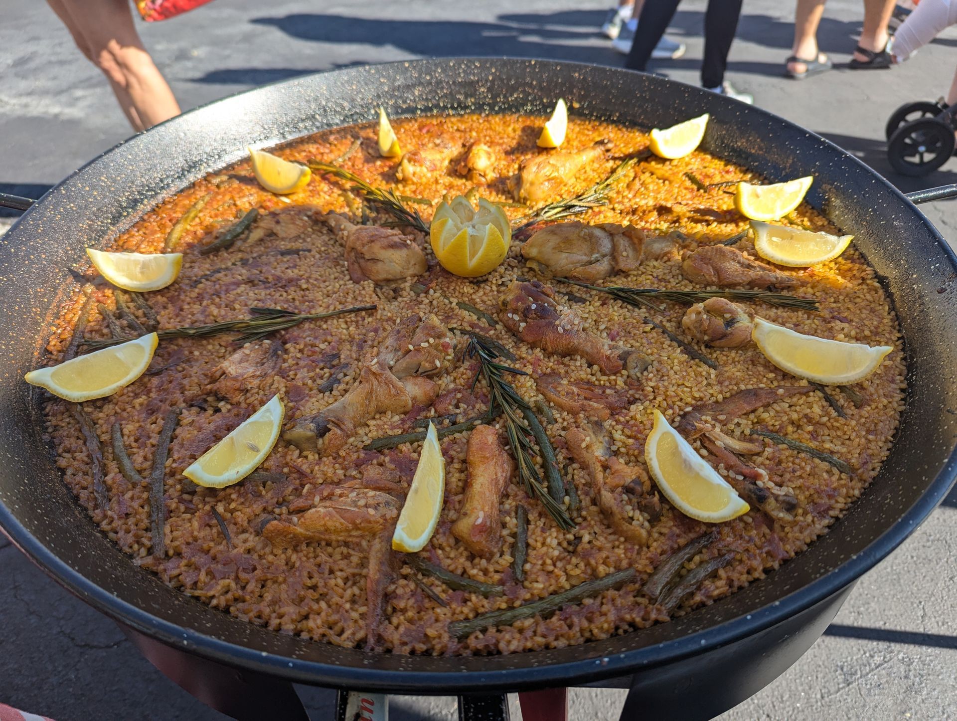 Large paella pan with chicken, vegetables, and lemon wedges catering
