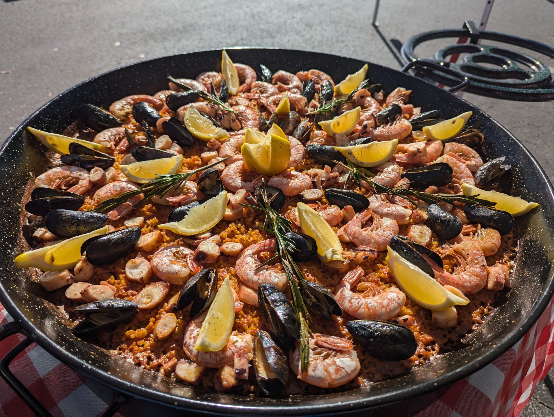 Paella with shrimp, mussels, and lemon wedges in a large pan on an outdoor burner catering