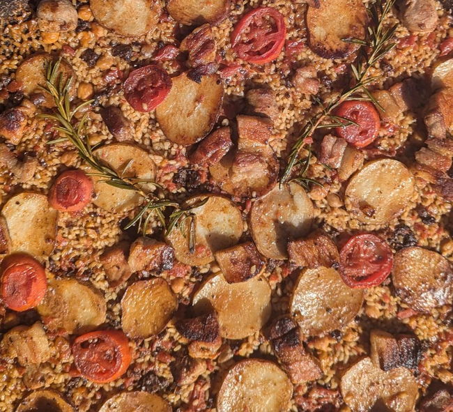 Paella in a large, round pan; includes potatoes, tomatoes, and meat.