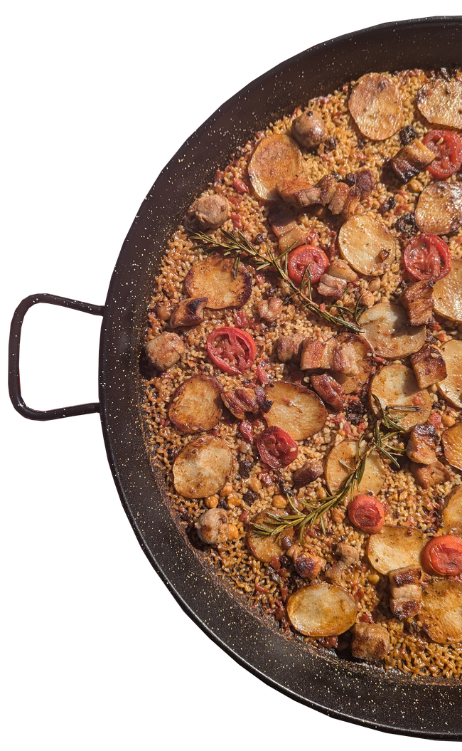 Paella in a large, round pan; includes potatoes, tomatoes, and meat.