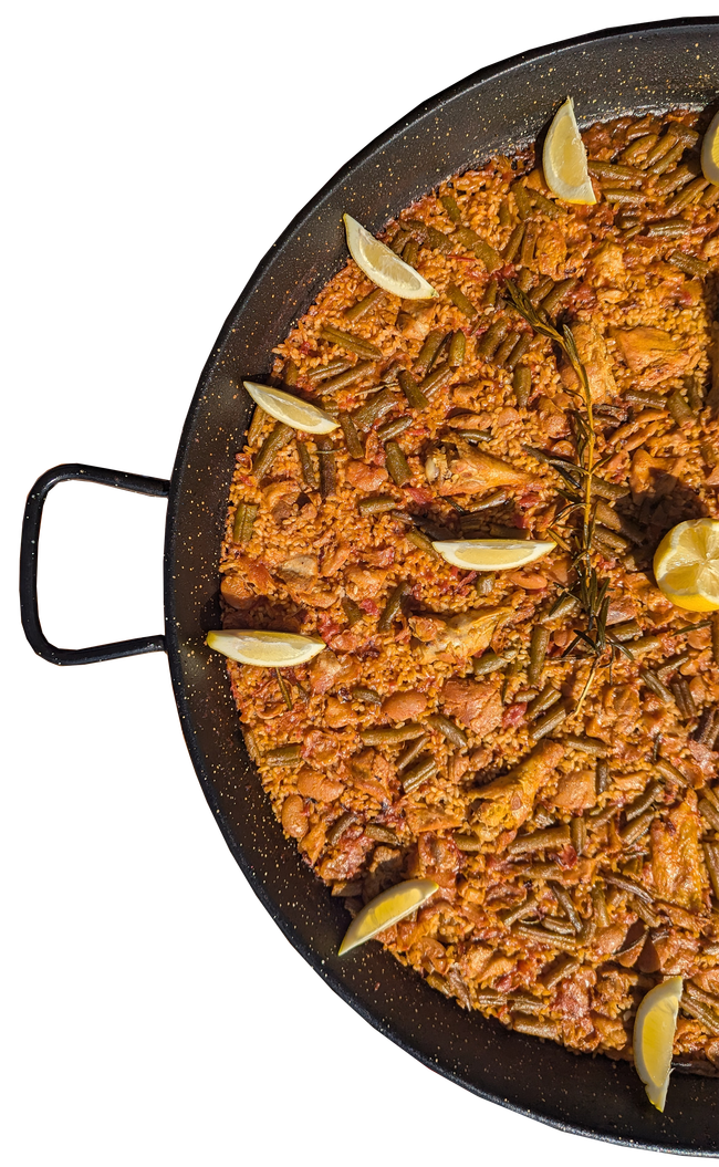 Paella in a large black pan, garnished with lemon wedges.