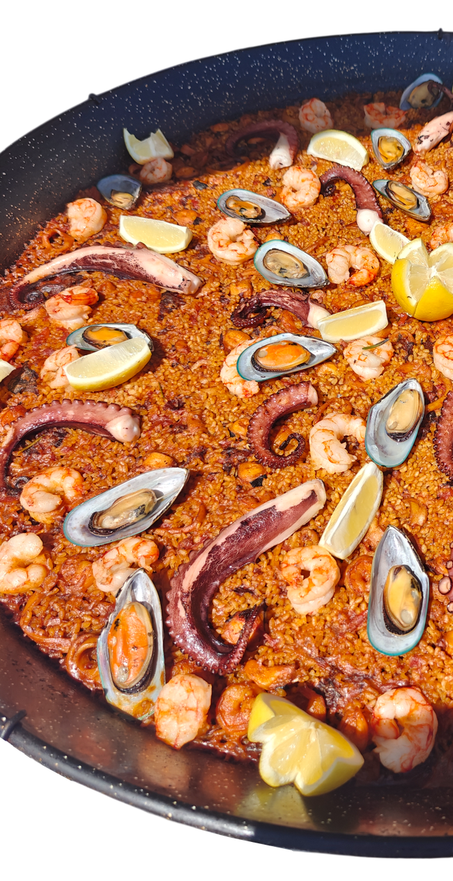 Paella with shrimp, mussels, and lemon wedges in a large, black pan.
