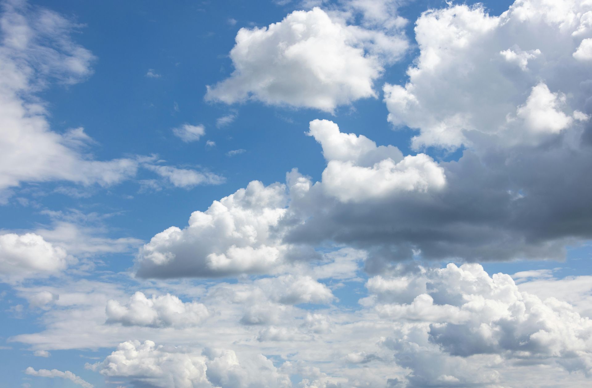 Blue sky with scattered white cumulus clouds and a large gray cloud formation