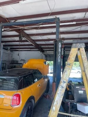 Yellow Mini Cooper in a garage beside a car lift and ladder