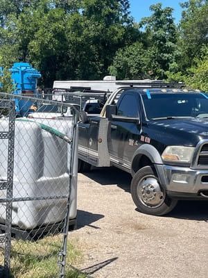 Flatbed truck with white tanks and metal cages parked outdoors beside trees.