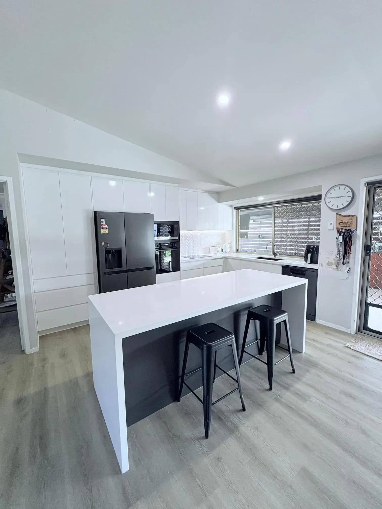 Modern kitchen with white cabinets, dark island, and black stools.
