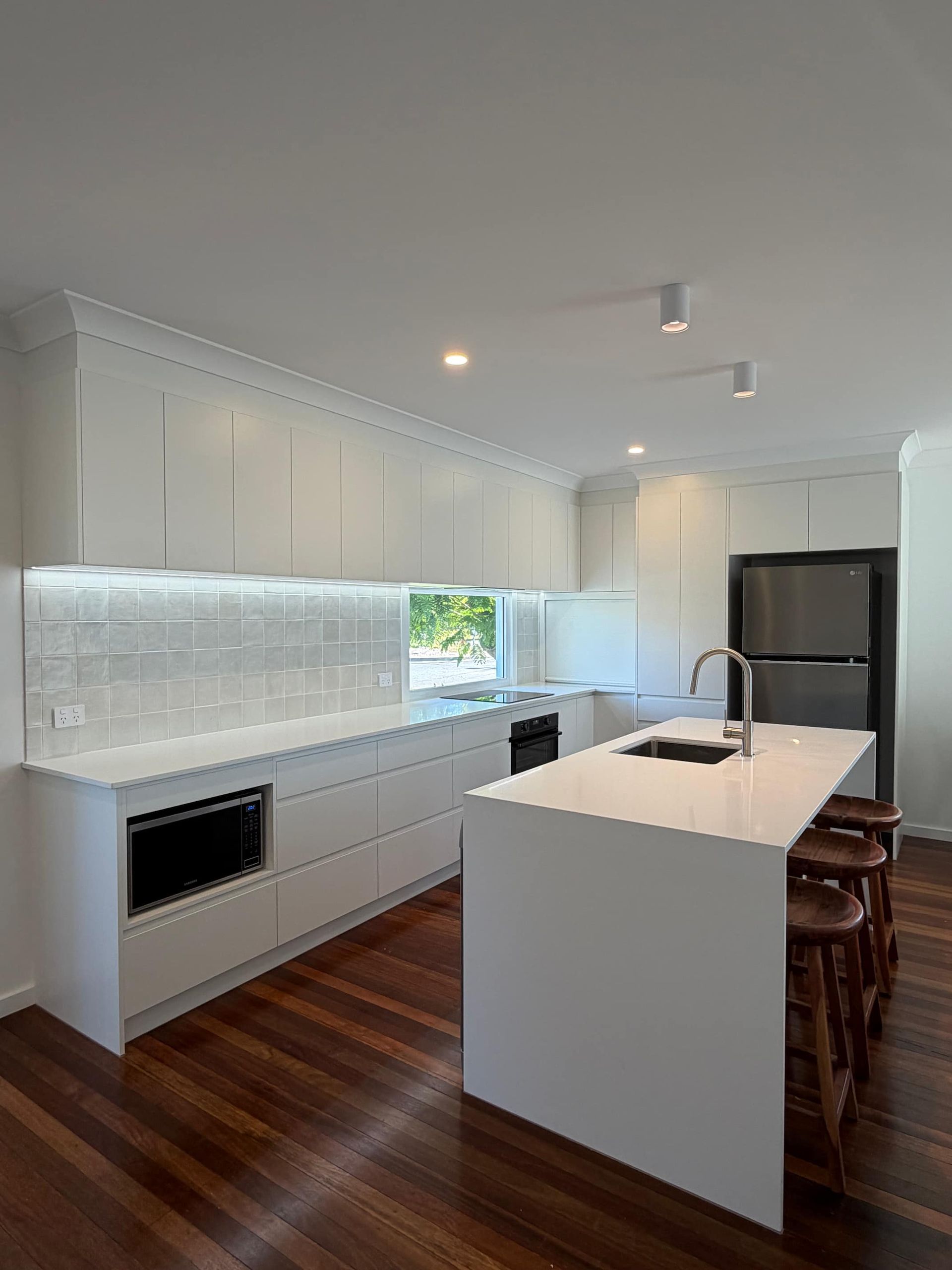 White modern kitchen with a large island, stainless steel appliances, and wooden floors.