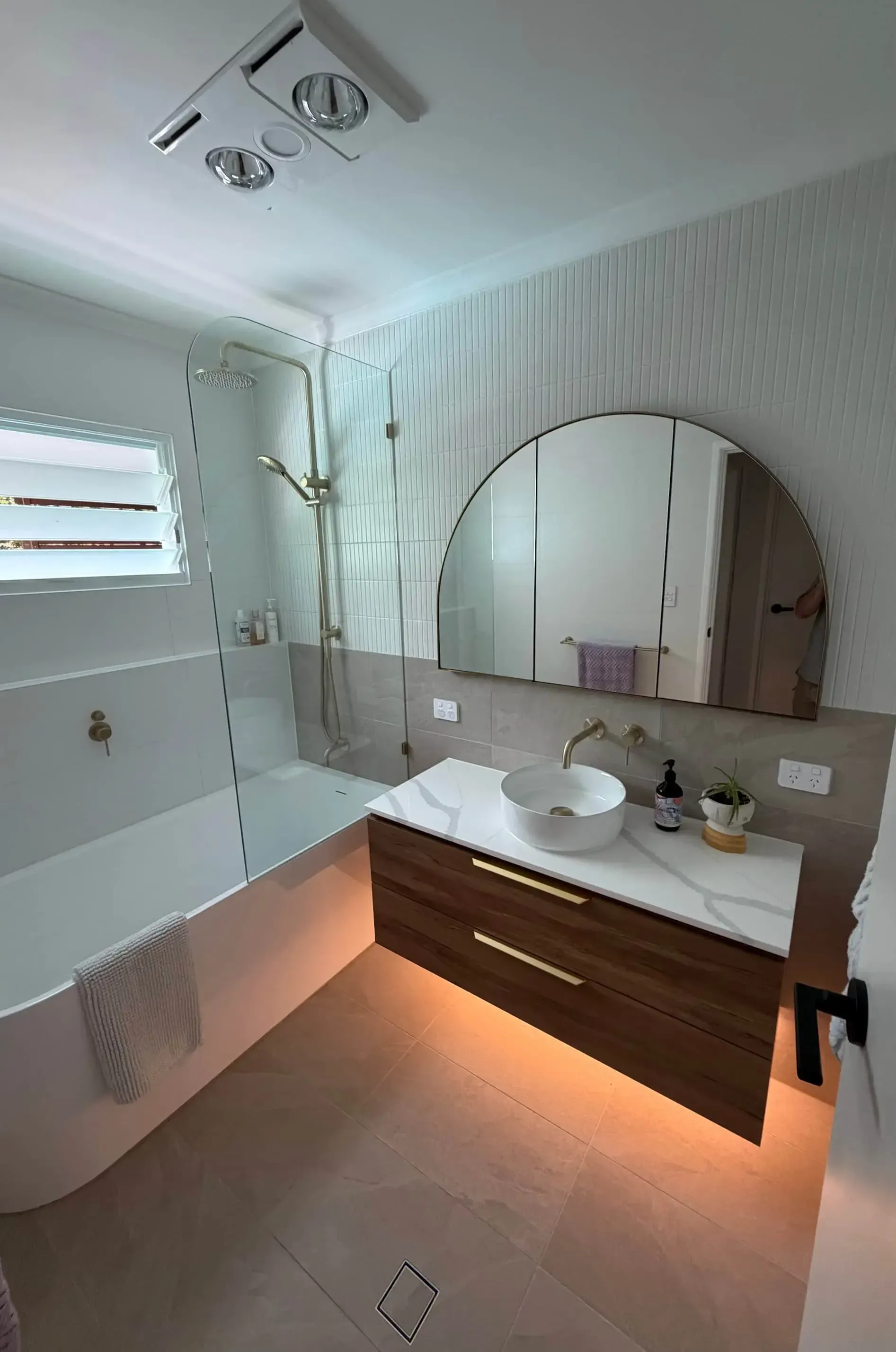 Modern bathroom with a bathtub, shower, vanity with a round mirror, and a wood cabinet.
