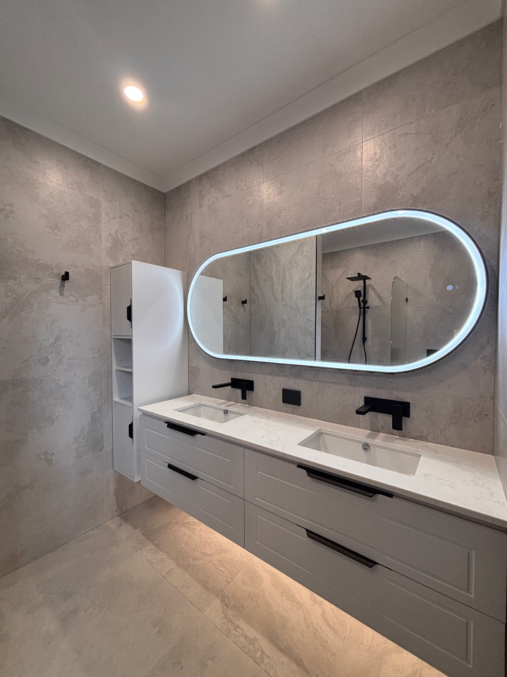 Modern bathroom with double sink vanity, oval illuminated mirror, and walk-in shower.