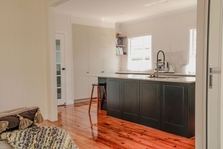 Bright kitchen with black island, white cabinets, hardwood floors, and a small table by the window