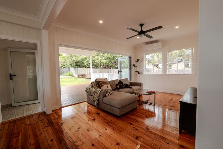 Bright living room with hardwood floors, gray sofa, ceiling fan, and open view to a patio and yard