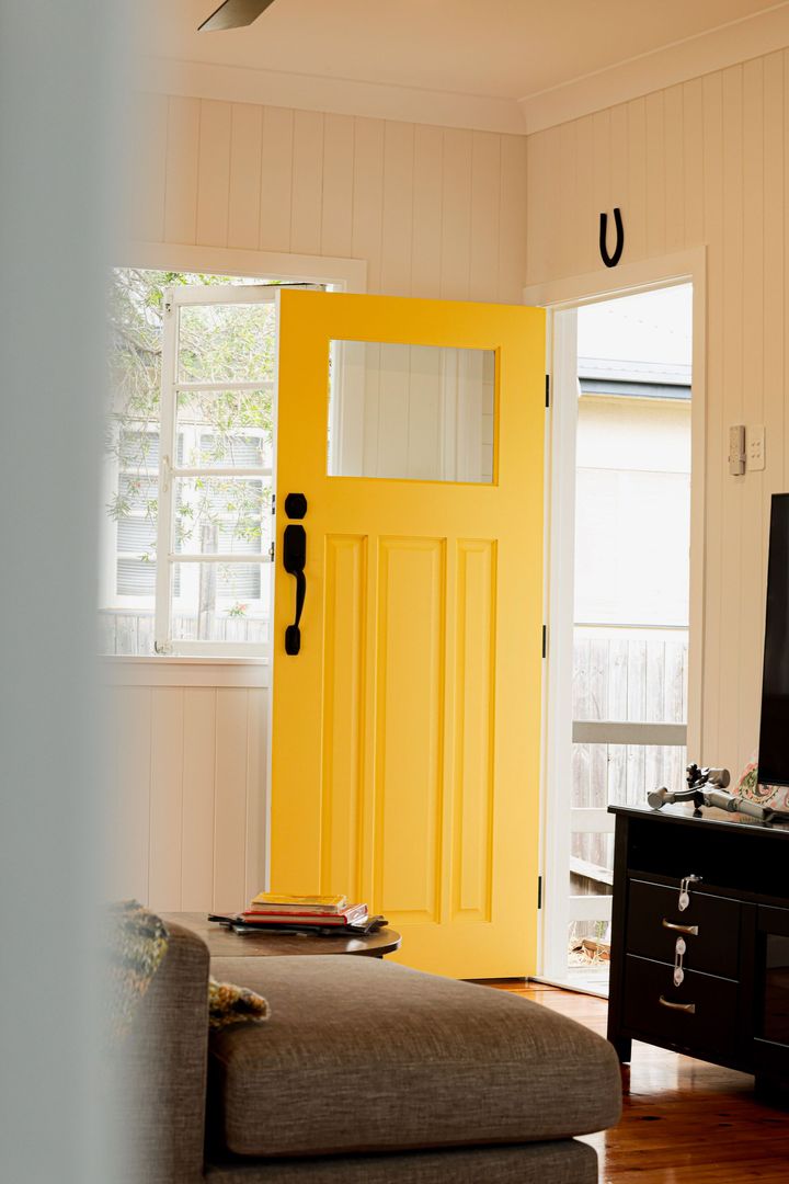 Bright yellow front door open in a cozy living room with a sofa and TV cabinet.