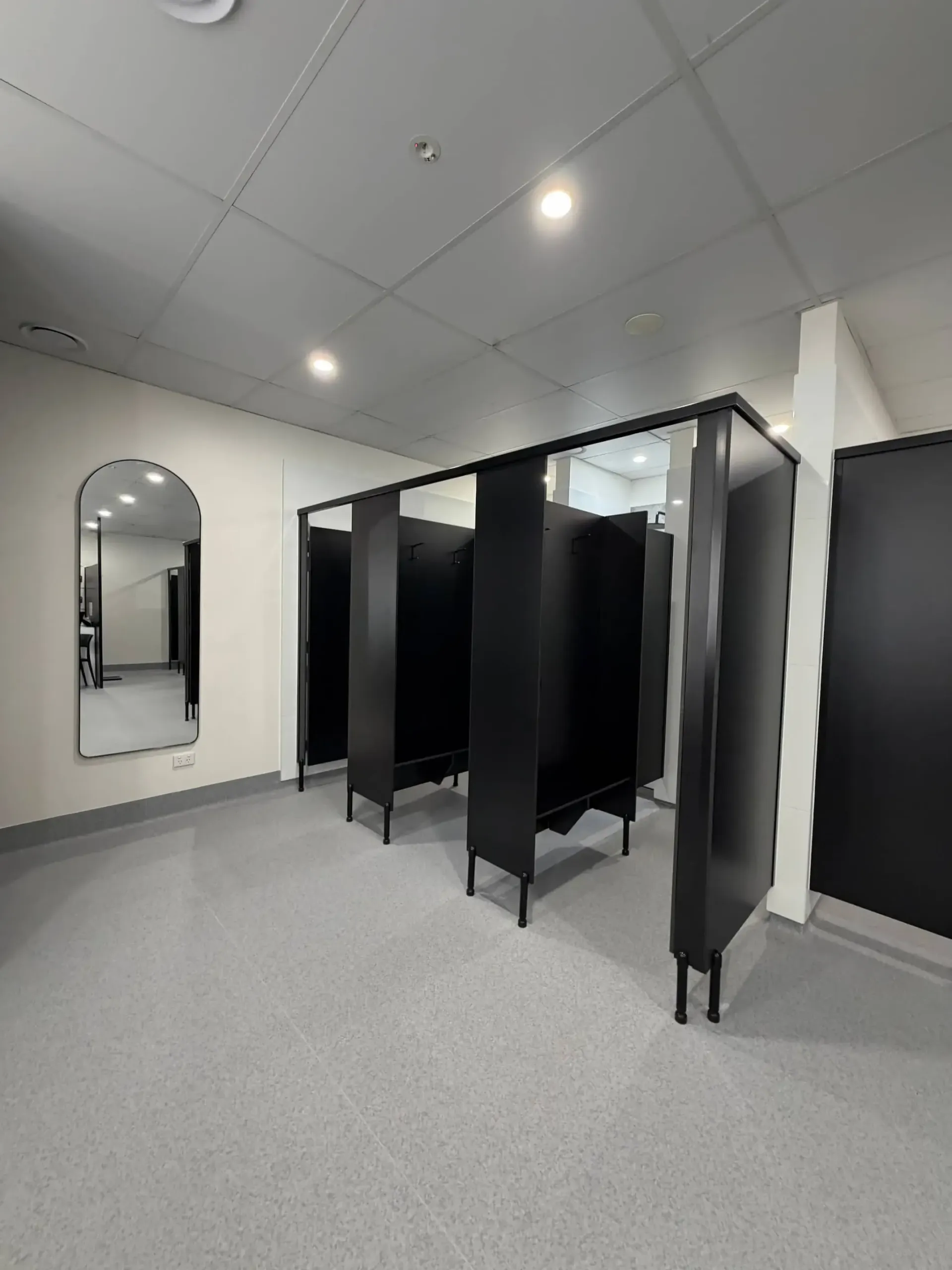 Modern restroom with black stalls, large mirror, and gray flooring.