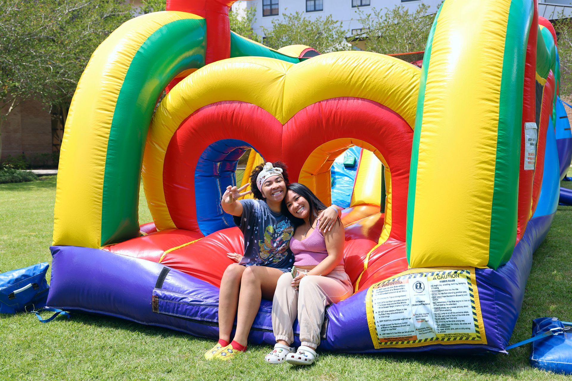 Two children sitting on a colorful inflatable bounce house in a grassy park