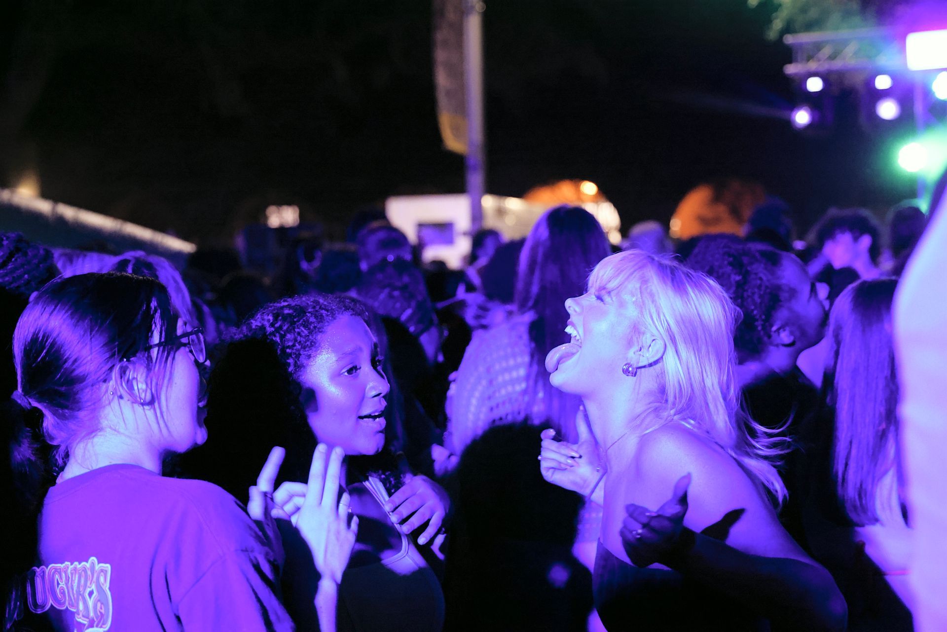 Crowd at a nighttime concert under purple stage lights, people talking and dancing