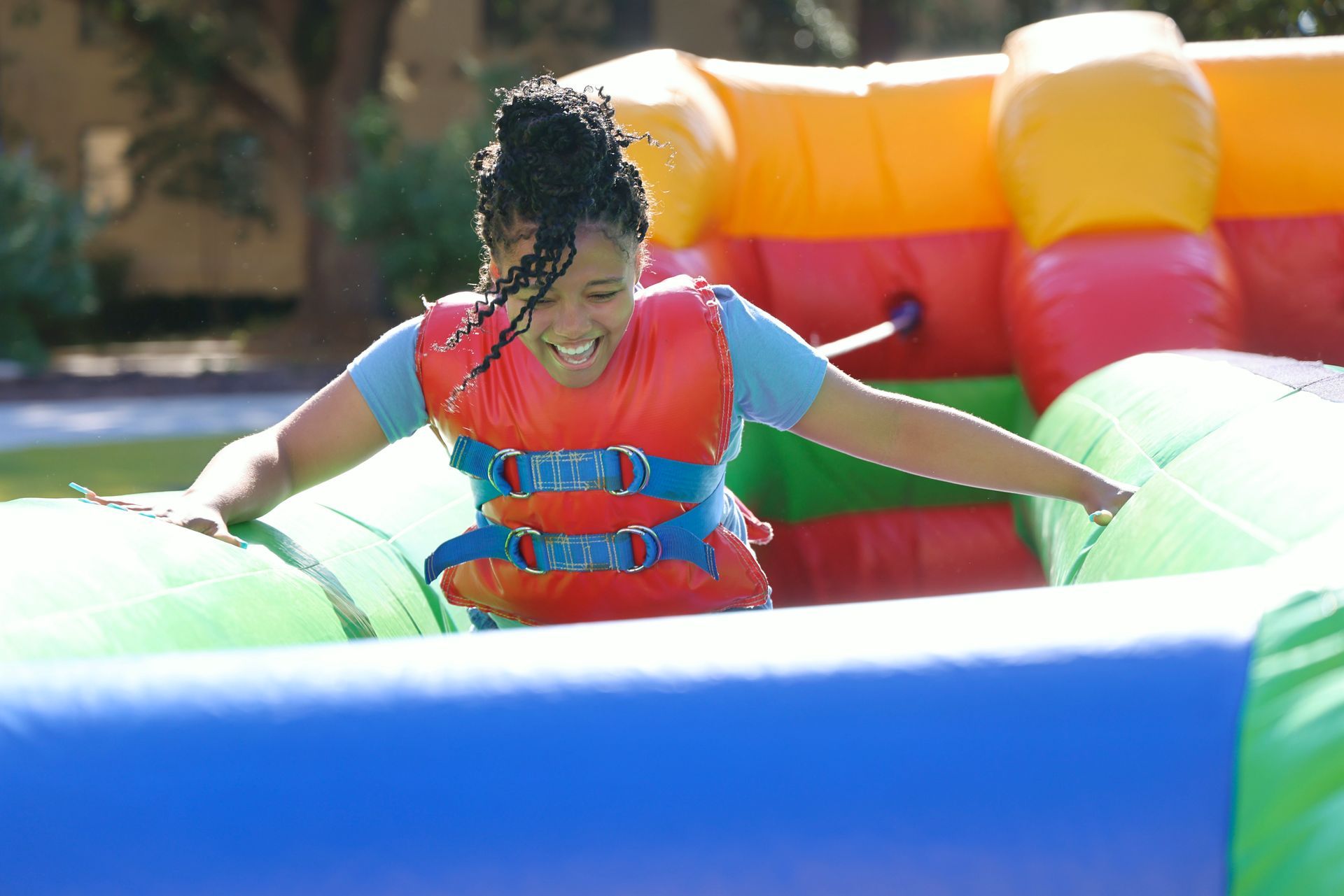Child in a red life vest playing in a colorful inflatable water attraction, arms outstretched and smiling.