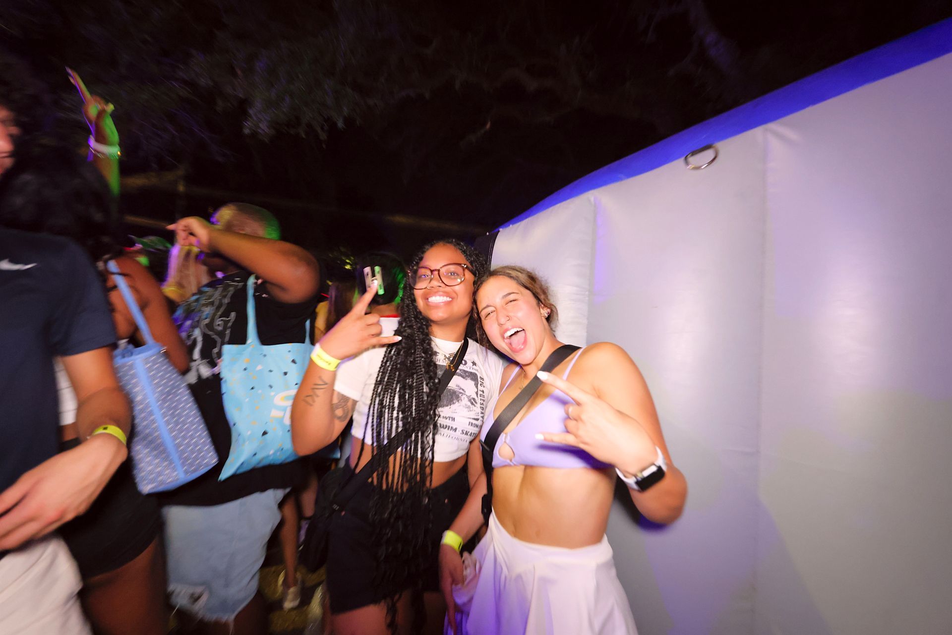 Two friends posing and smiling at a nighttime party, one in a black dress and one in a white top and skirt.