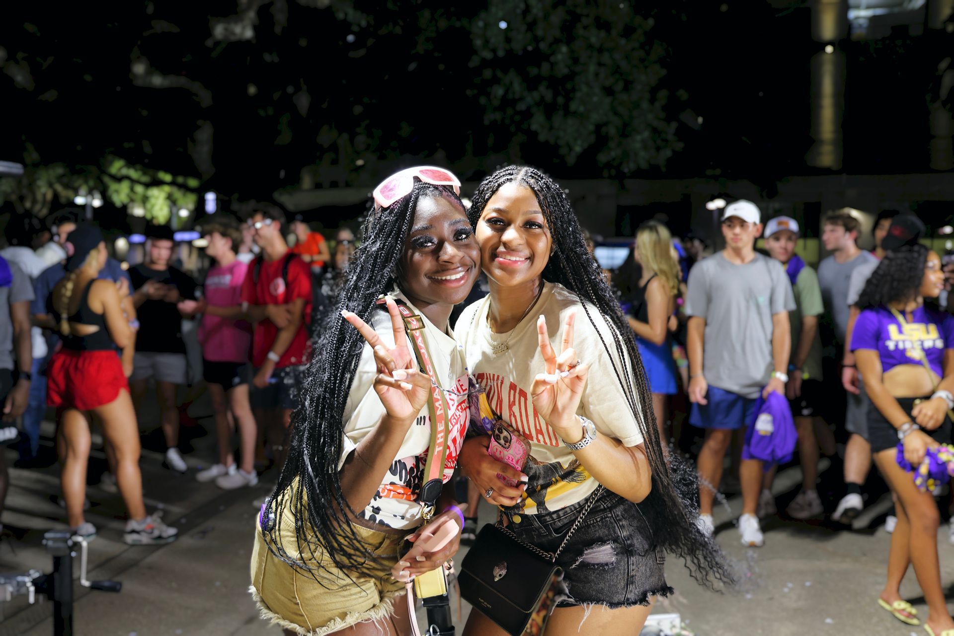 Two smiling people posing and flashing peace signs at a crowded night street event