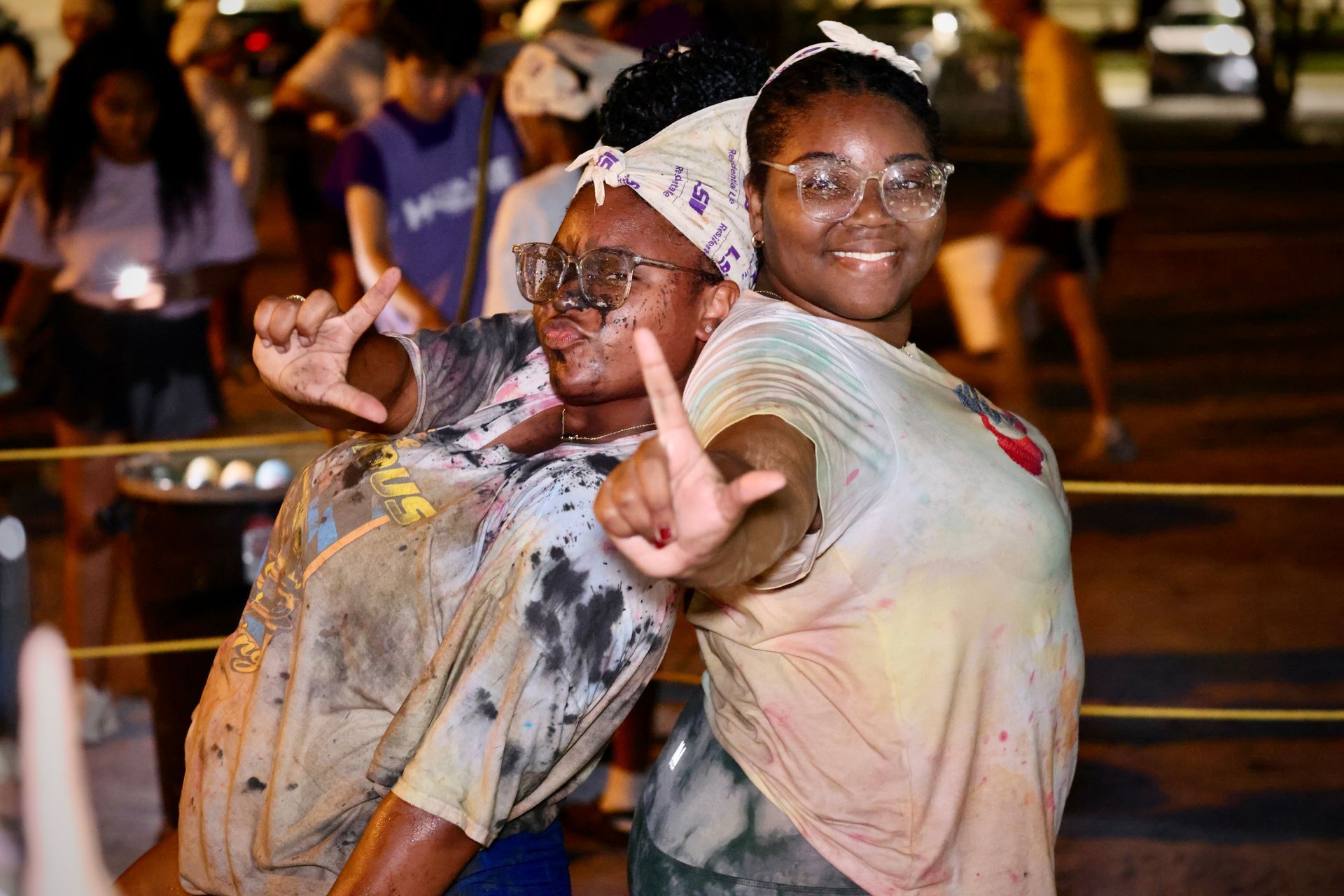 Two people smiling and posing at a night street event, one making a peace sign