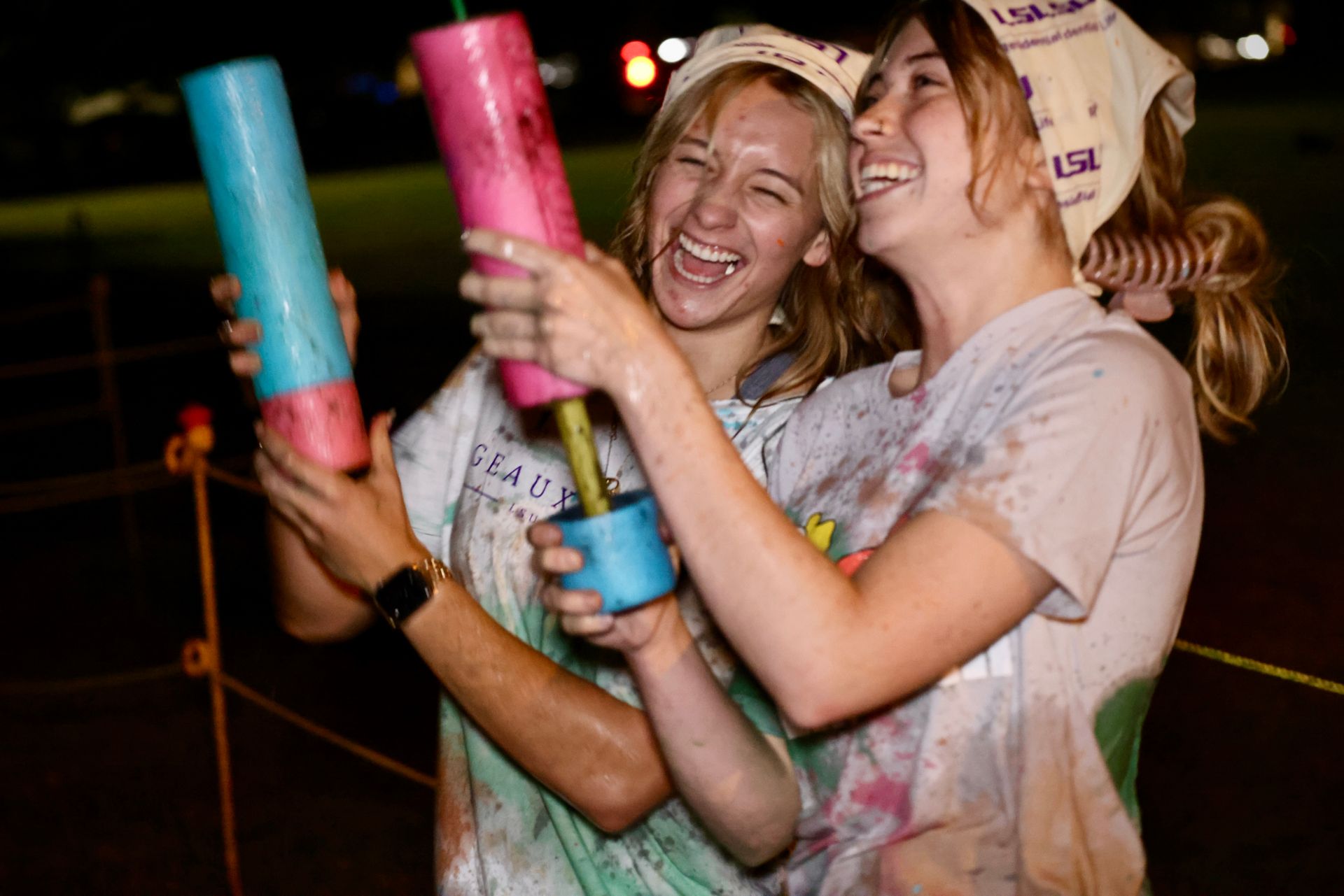 Two smiling people holding colorful confetti tubes at a nighttime celebration