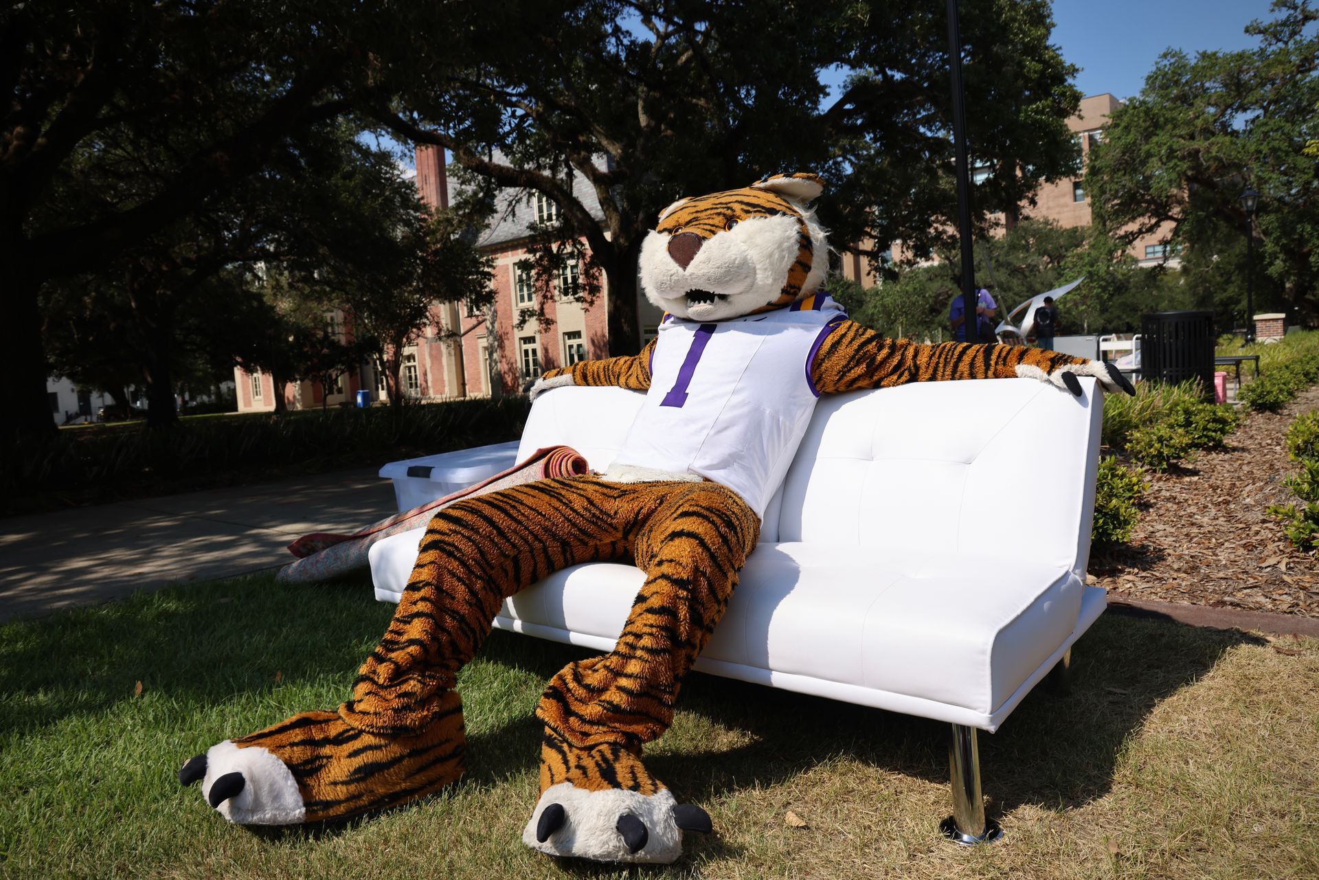 Large tiger mascot lounging on a white couch outdoors on a sunny lawn
