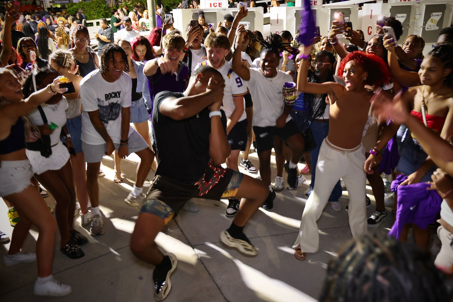 People dancing energetically in a crowded outdoor street celebration with raised arms and colorful outfits