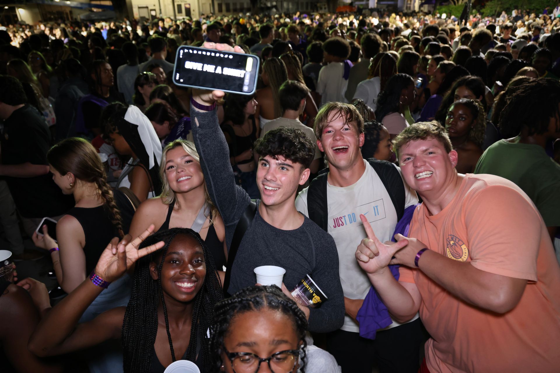 Crowded event with a group of smiling people posing for a selfie under bright lights