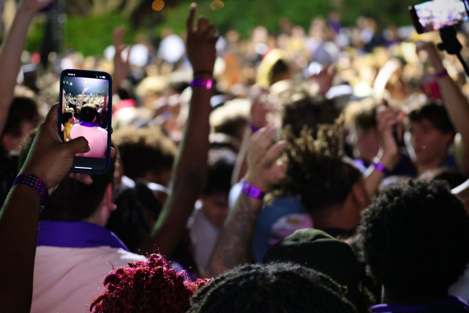 Crowd at an outdoor event, with raised hands and a smartphone recording the scene