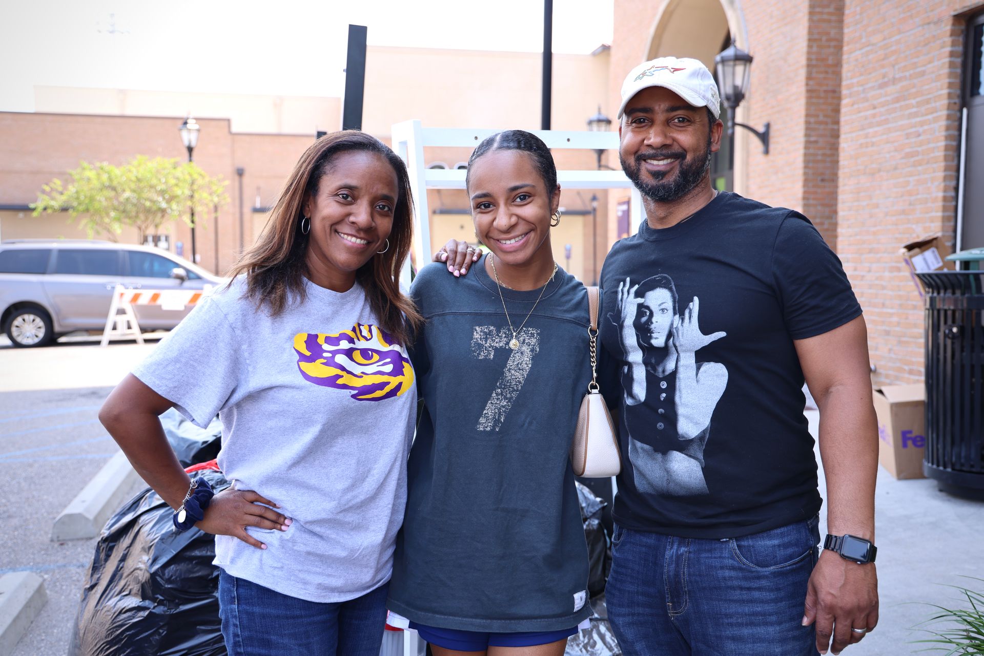 Three people smiling outdoors, standing together in front of a brick building.