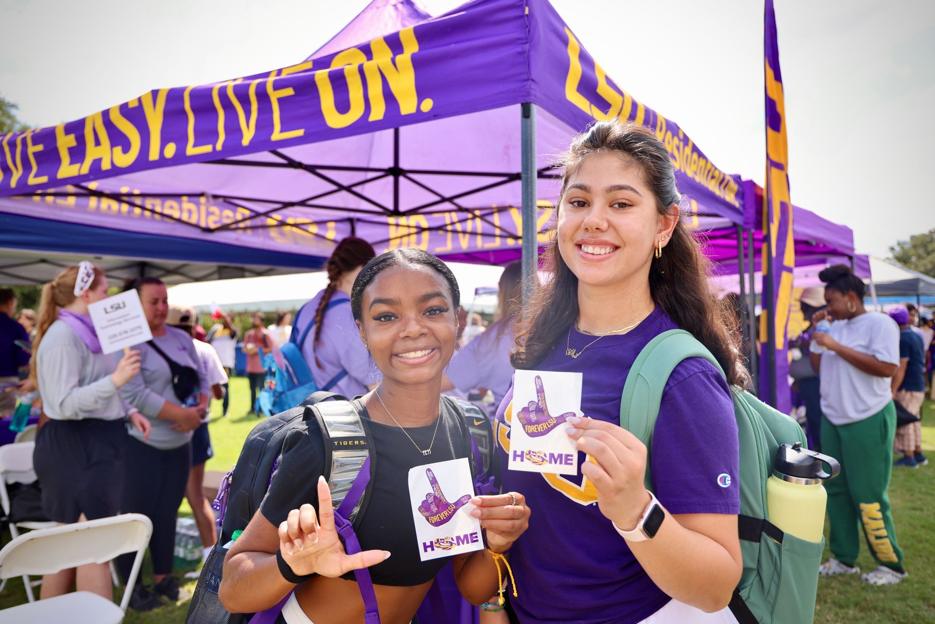 Two smiling students in purple shirts pose at a campus booth under a purple canopy.