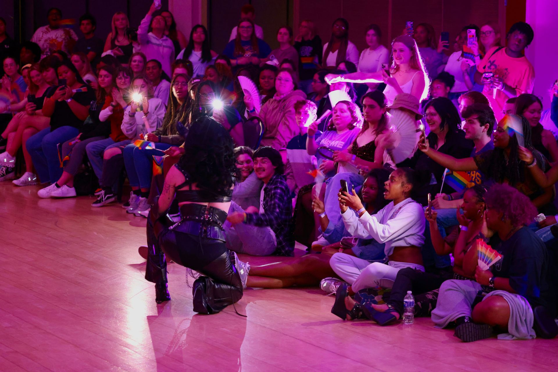 Dancer performing on a pink-lit stage in front of a seated audience, some holding cameras