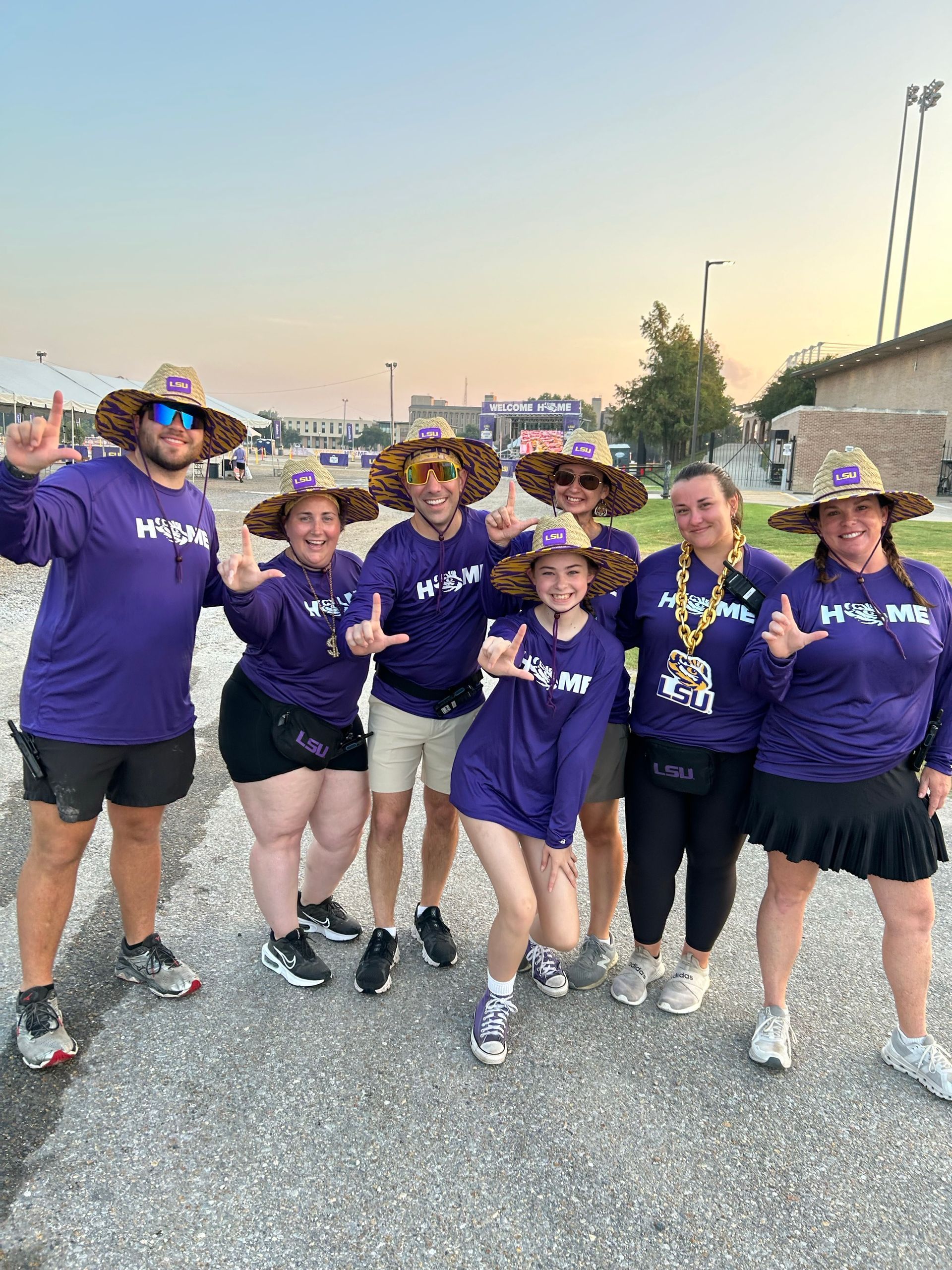 Group of people in purple shirts posing together outdoors on a gravel road at dusk.