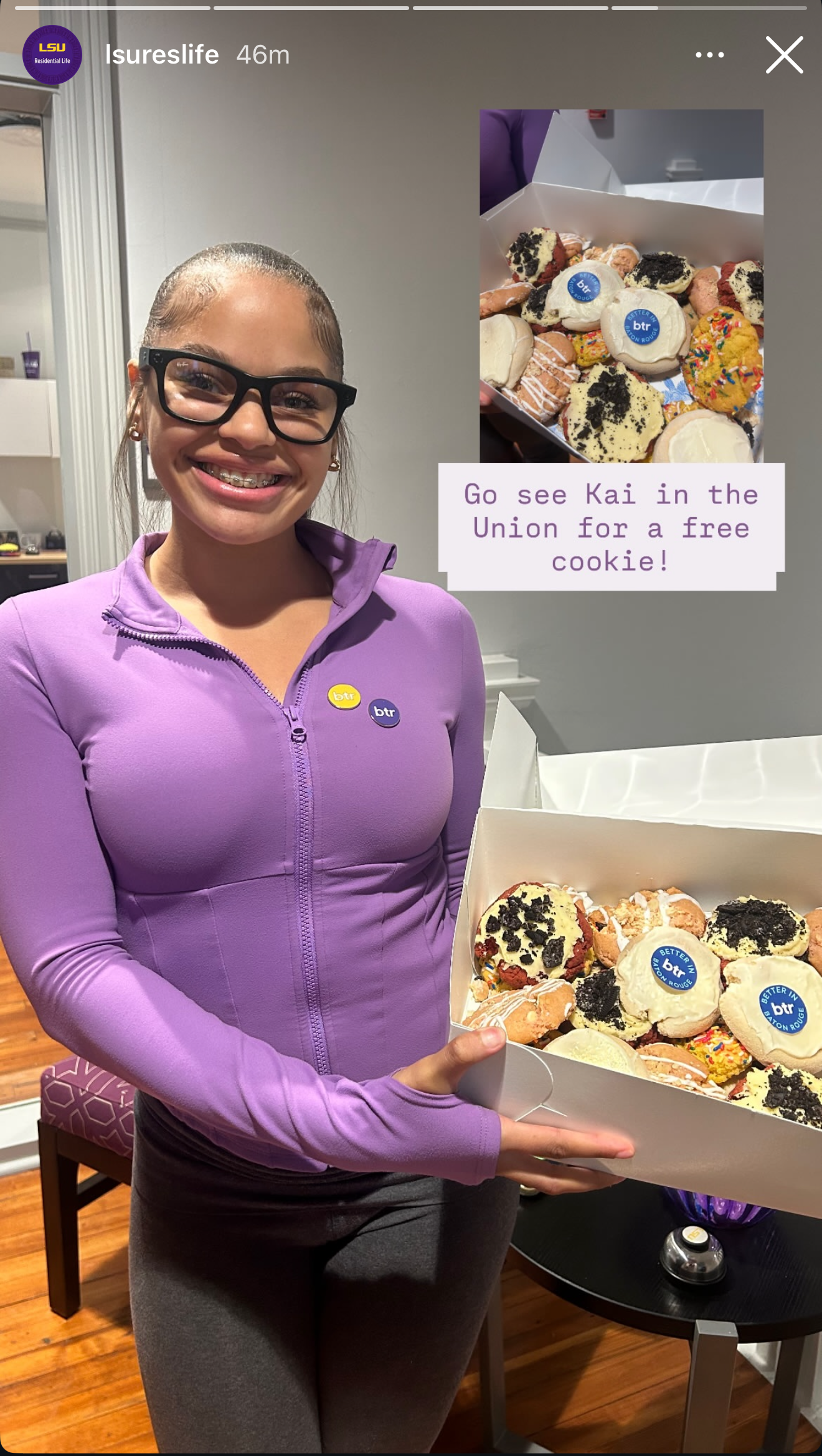 Woman in purple top smiling beside a display of decorated pastries with a note sign.