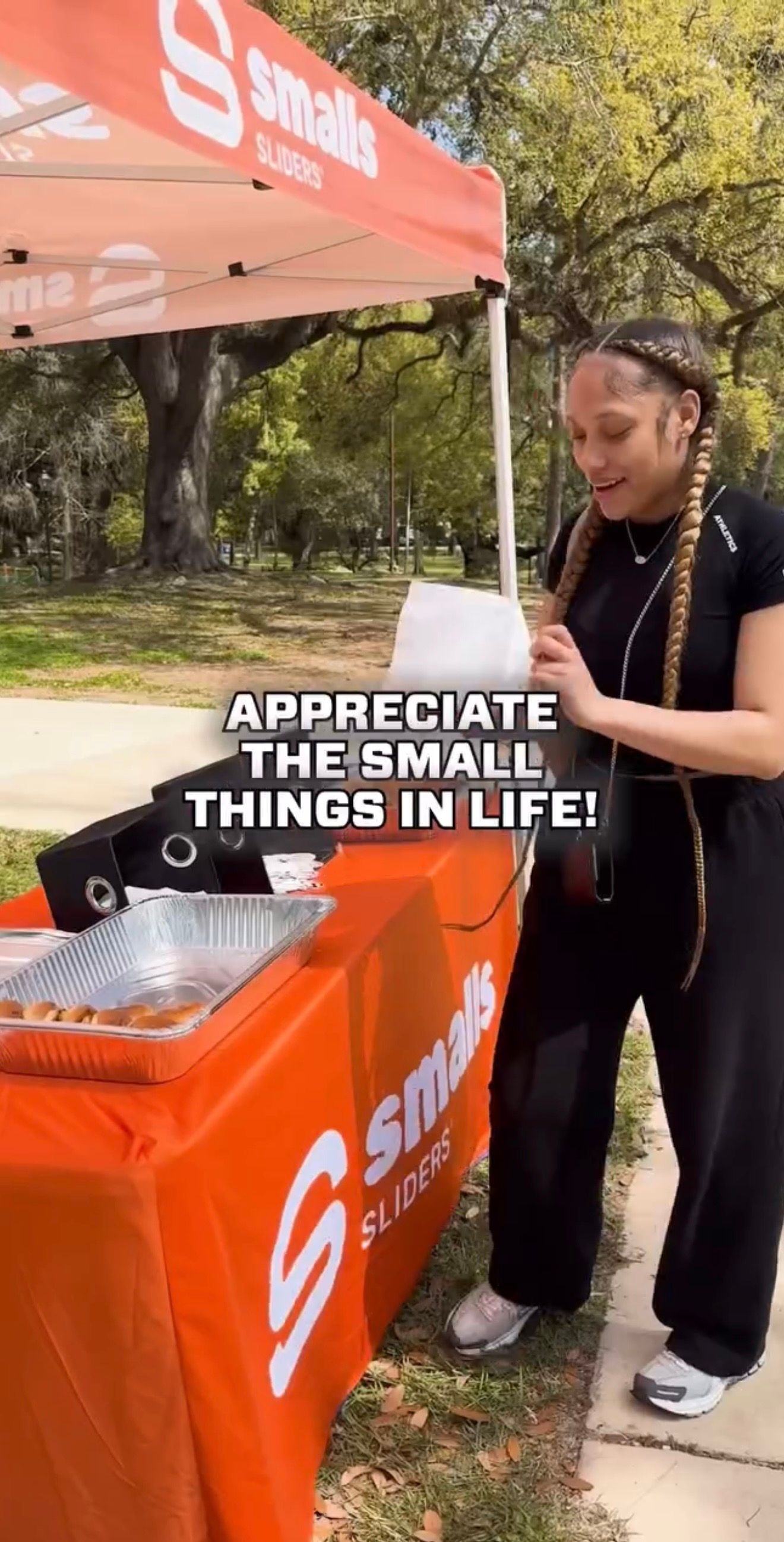 Woman standing beside an orange Smalls table at an outdoor event, with text reading “Appreciate the small things in life.”