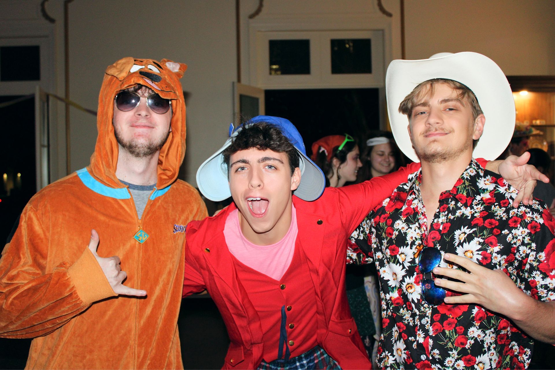 Three people in colorful costumes posing together at a party, one with arm around the others.