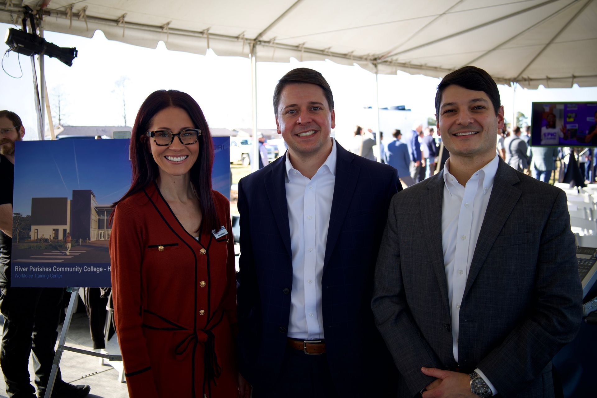 Three people posing under a white tent, smiling beside a poster display.