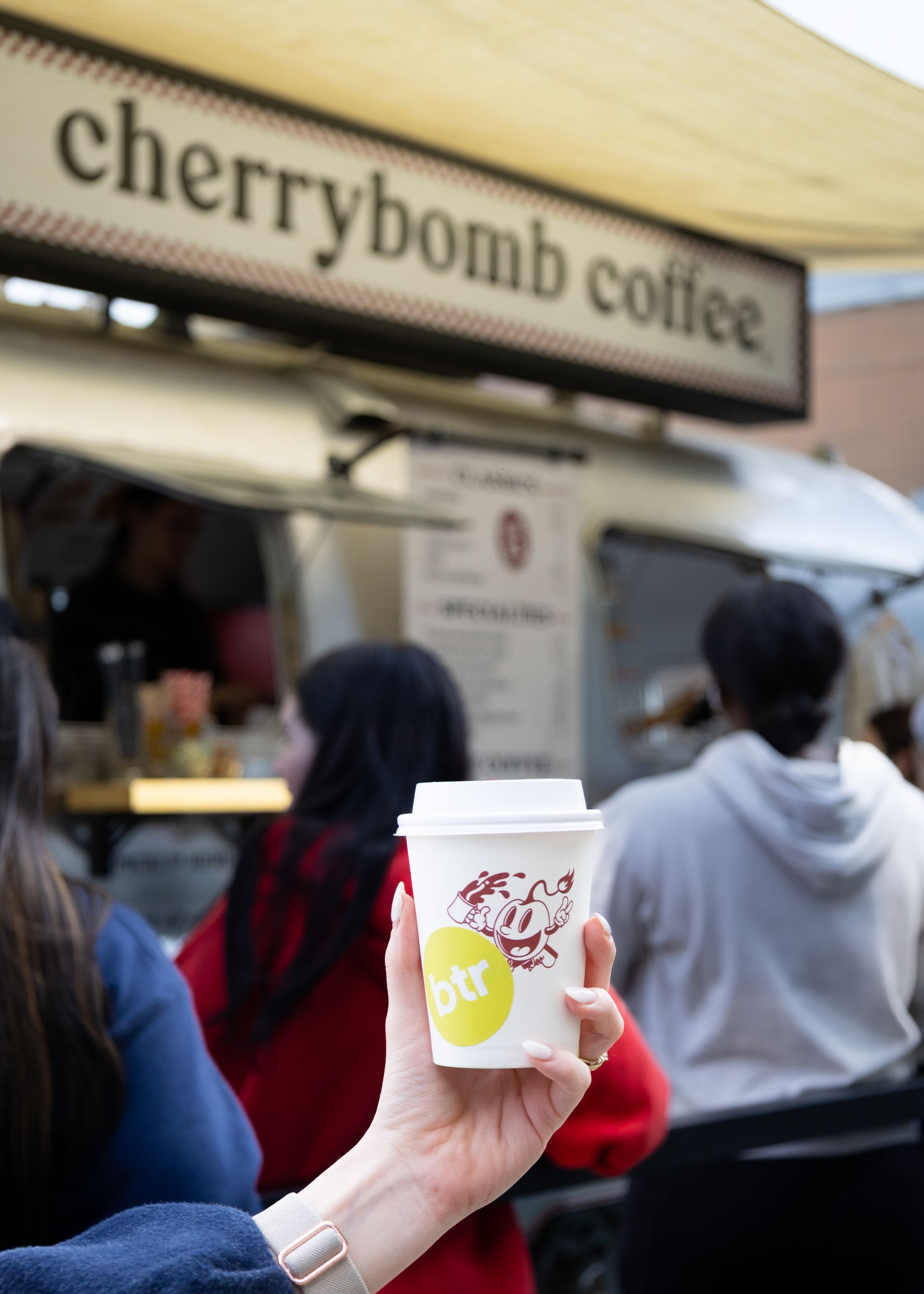 Hand holding a white takeaway cup at a Cherrybomb Coffee food truck counter
