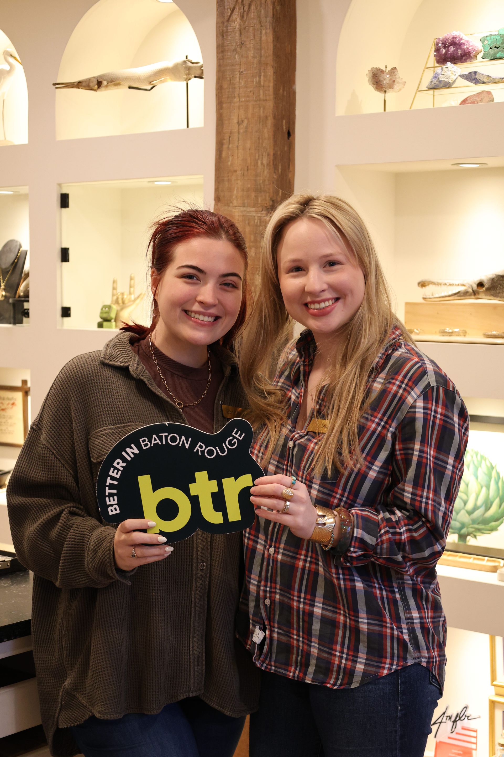 Two smiling people holding a black-and-yellow “btr” sign in a bright store display area