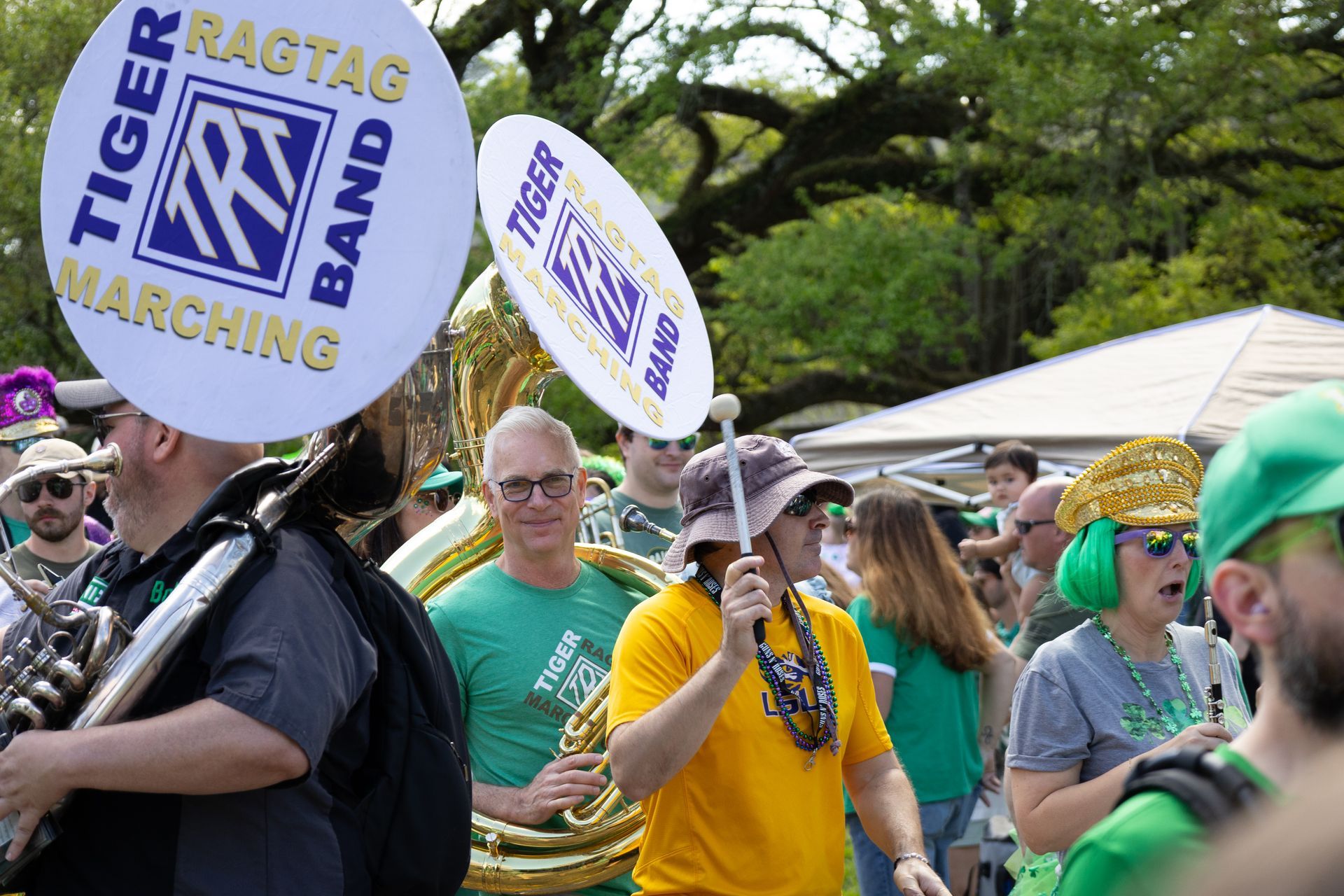 Marching band members in green and yellow costumes carrying round “Tiger Ragtime” signs outdoors
